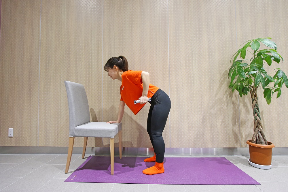 足は腰幅に開き、膝を軽く曲げて、前かがみの姿勢をとる。片手をウエイトベンチや安定した椅子につき、もう片手でダンベルなどの重りを持ち、肘を曲げた位置で構えます。